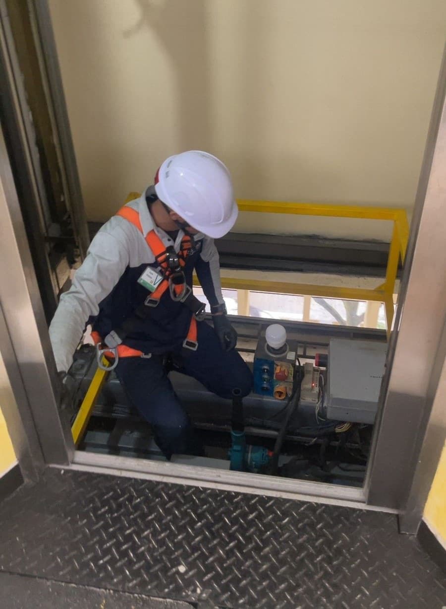 Técnico de Quantium con casco y arnés de seguridad realizando mantenimiento preventivo en el foso del ascensor