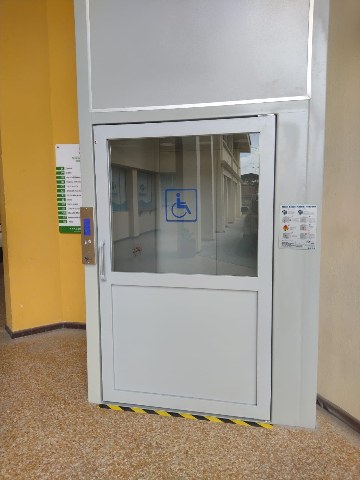 Puerta de la plataforma salvaescaleras con símbolo de accesibilidad y botonera instalada en la Gobernación del Cauca