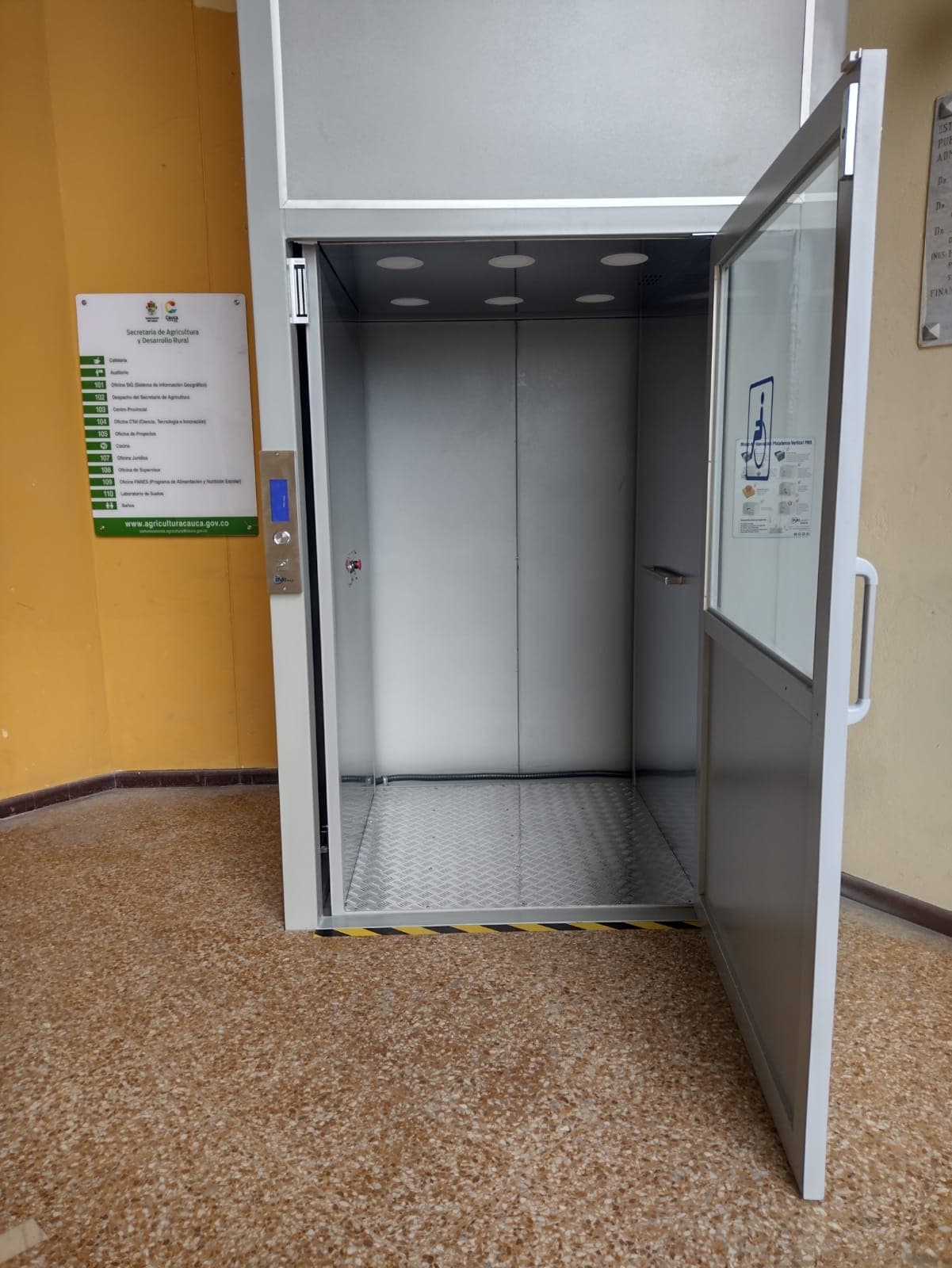 Cabina de la plataforma vertical con puerta abierta, piso antideslizante e iluminación interior en la Gobernación del Cauca