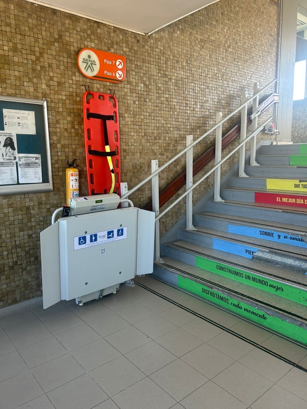Plataforma salvaescaleras plegada junto a las escaleras con mensajes de colores del SENA en Barranquilla
